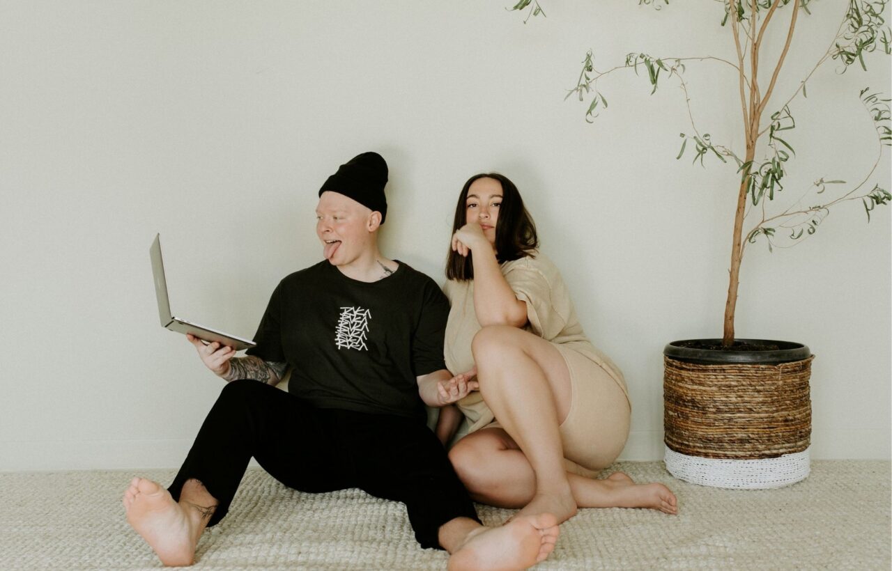 Couple sitting on a cozy rug with a laptop beside a potted tree, suggesting relaxed conversation starters for partners at home.