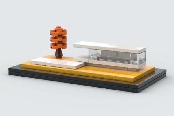 Miniature LEGO-style modern house model with orange tree on a yellow and black display base against a gray background.