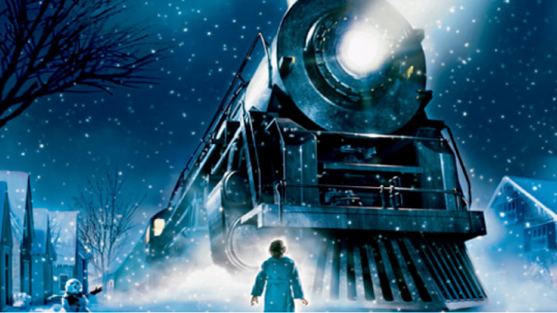 The Polar Express steam train arrives in a snowy village at night as a child stands before its glowing headlight.
