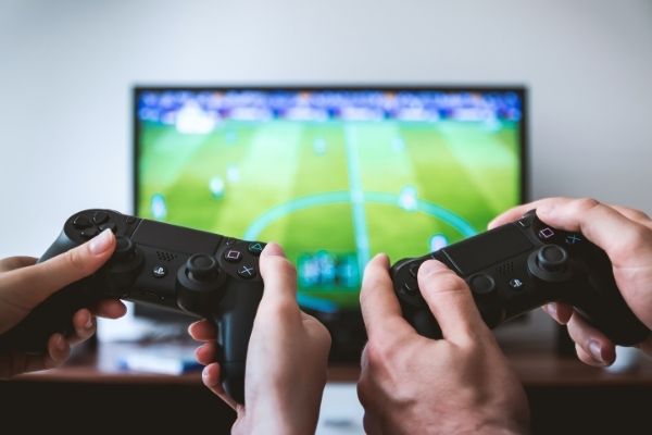 Two people holding PlayStation controllers while playing a soccer video game on a TV, a cozy at-home date night gaming activity.