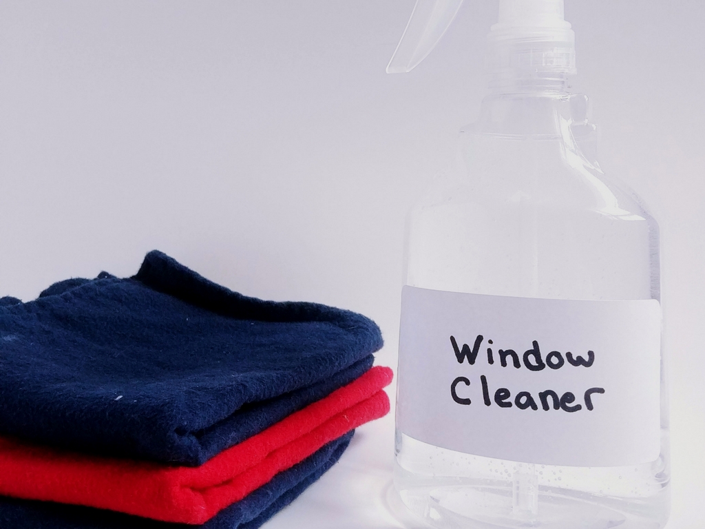 Spray bottle labeled window cleaner beside folded microfiber cloths for homemade eco-friendly glass cleaning