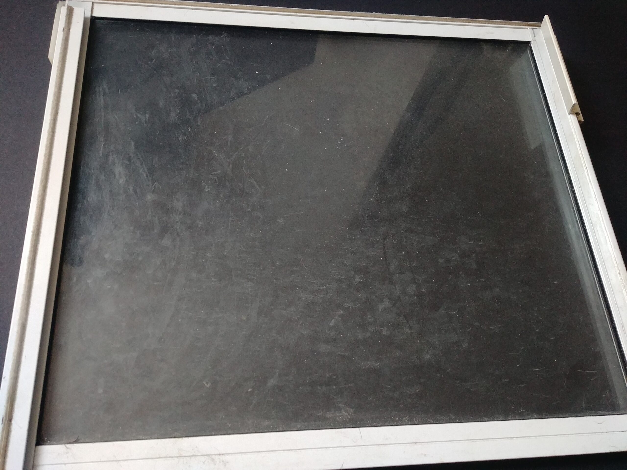 Dirty window pane in a white frame, showing cloudy smudges and streaks before cleaning with homemade glass cleaner.