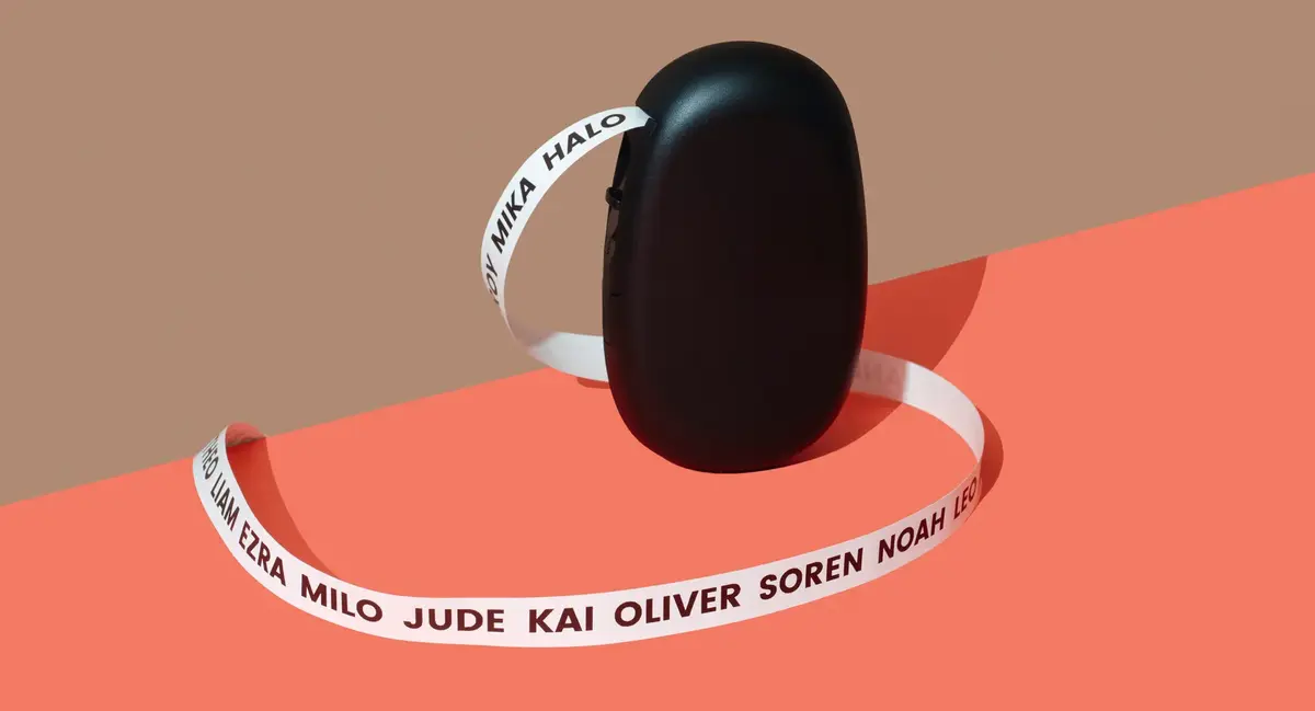 Black baby name label maker printing a long white ribbon of names on a coral and beige background