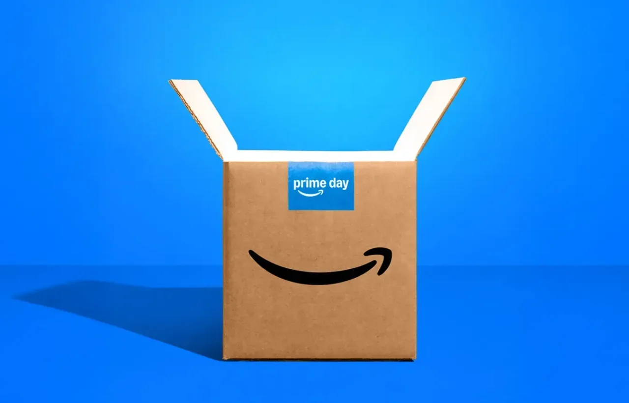 Open Amazon Prime Day cardboard delivery box on a bright blue background, highlighting shopping deals for baby products and essentials.