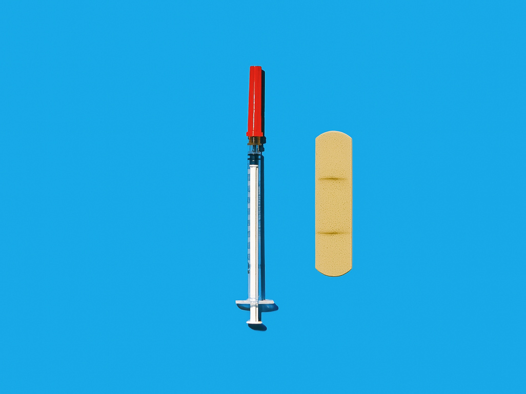 Syringe with a red cap and adhesive bandage on a bright blue background, representing the Tdap vaccine during pregnancy.