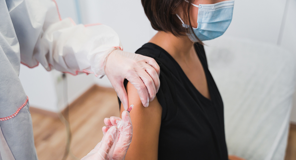 Pregnant woman wearing a face mask receives a vaccine from a gloved healthcare worker in a clinical setting.