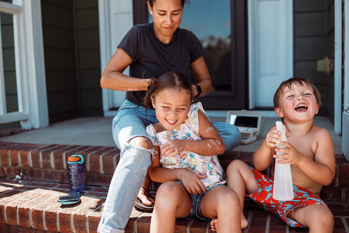 Mother helping her daughter on porch steps while a young boy laughs nearby, capturing playful family moments and everyday parenting.
