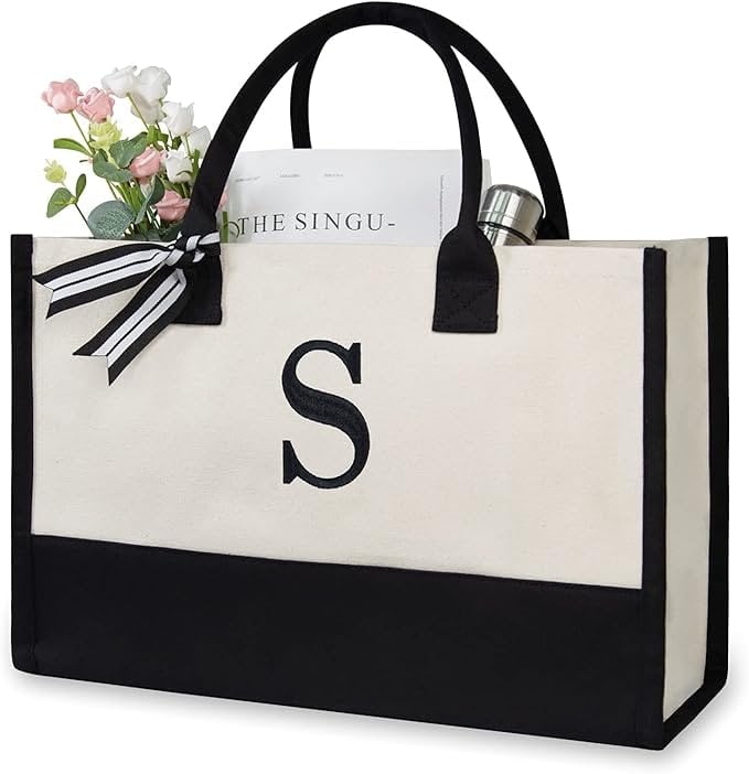 Monogrammed canvas tote bag with black handles, black trim, striped bow, flowers, book, and bottle tucked inside.
