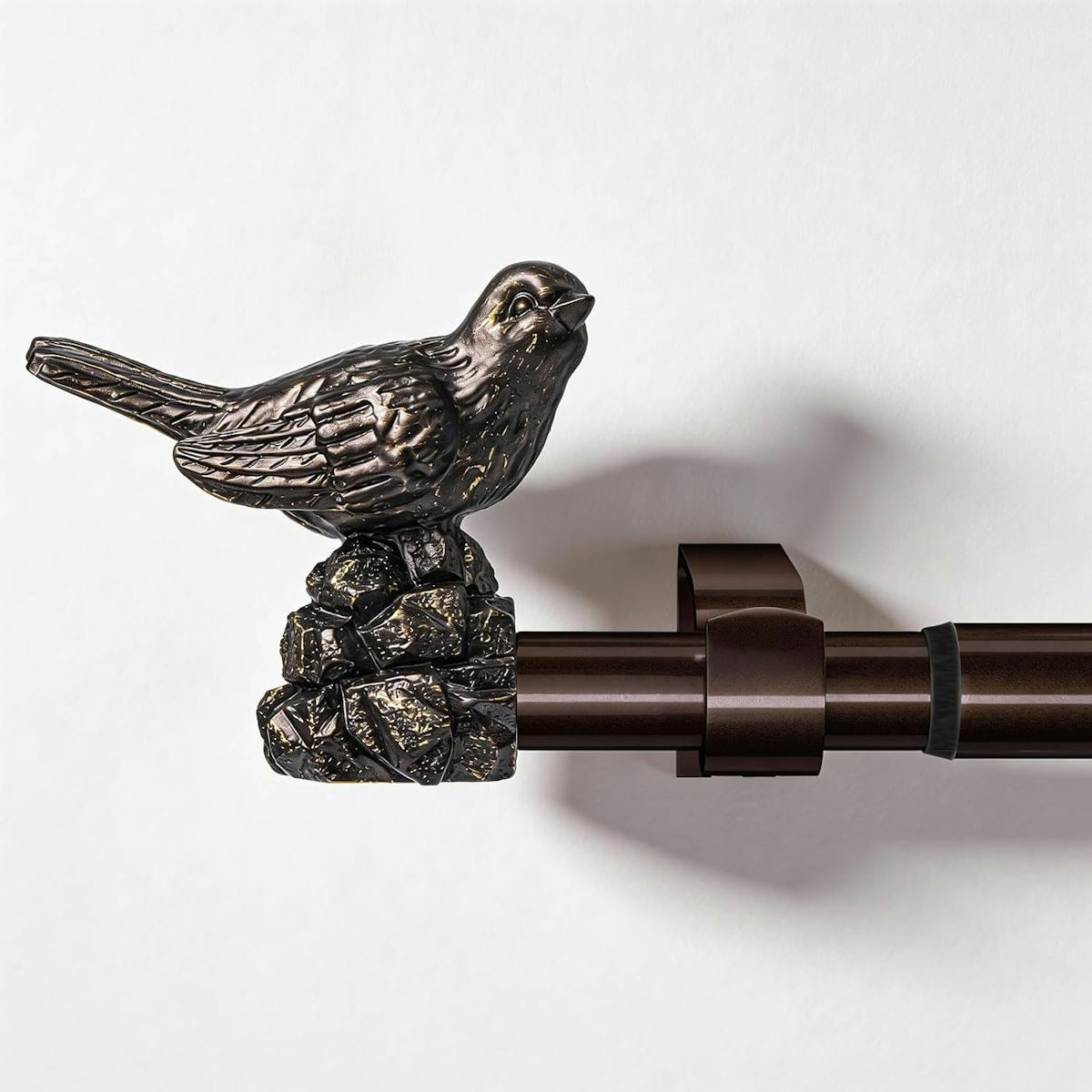 Oil-rubbed bronze curtain rod with a decorative bird finial mounted on a white wall for an elegant home decor accent.