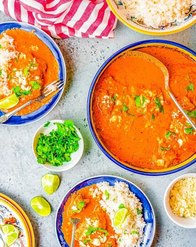 Creamy chipotle chicken in a tomato-based sauce served with white rice, lime wedges, cilantro, and cheese on colorful plates.