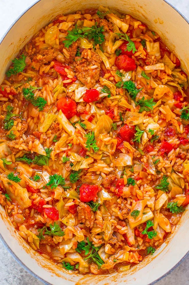 One-pot unstuffed cabbage rolls with rice, ground meat, tomatoes, cabbage, and parsley simmering in a Dutch oven.