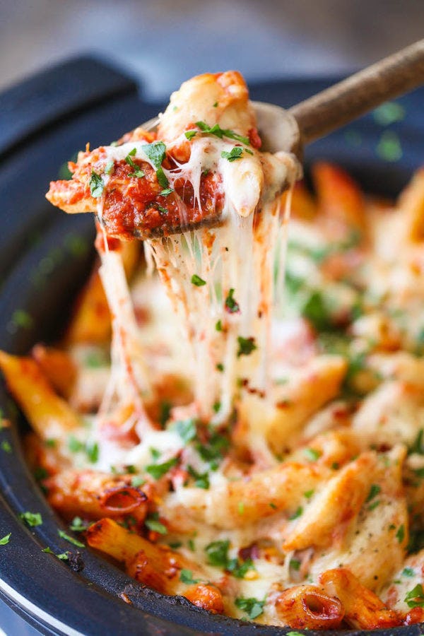 Cheesy baked pasta in tomato sauce lifted from a skillet with stretchy melted mozzarella and fresh parsley garnish.