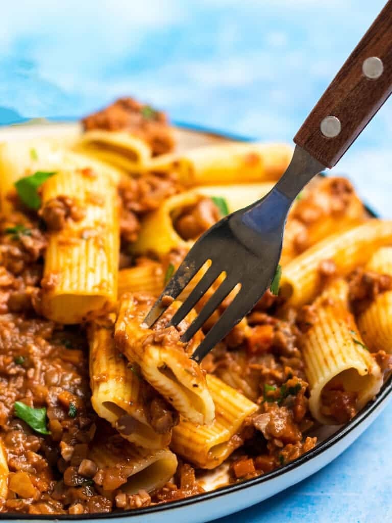 Close-up of rigatoni pasta coated in hearty tomato meat sauce with a fork lifting a bite, a comforting canned tomato dinner idea.
