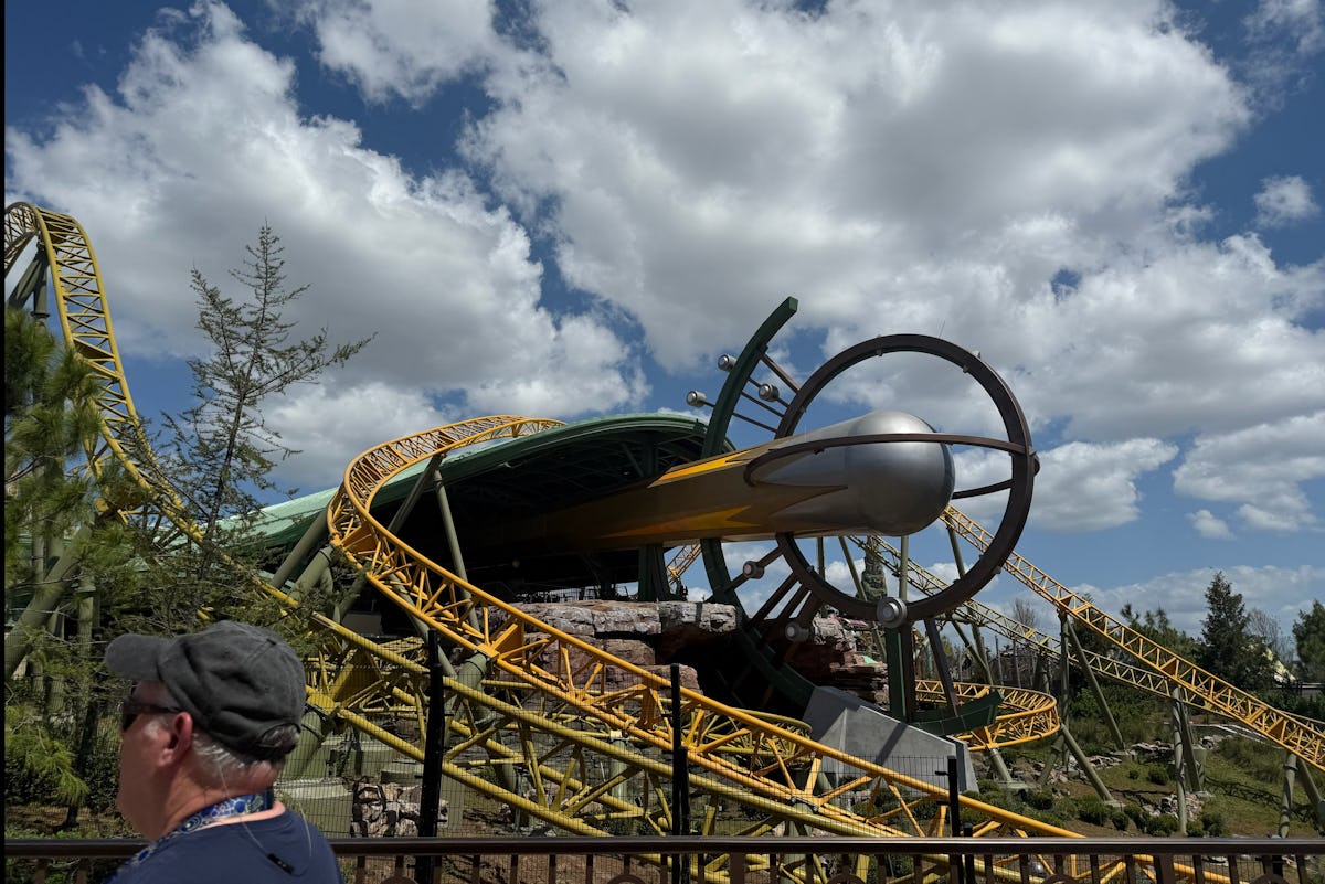 Yellow roller coaster tracks and a futuristic ride structure at Universal Epic Universe under a cloudy blue sky.