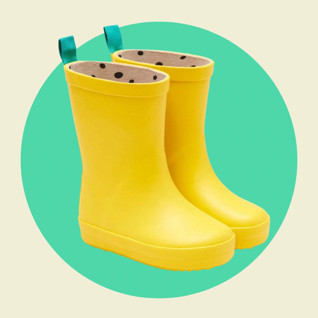 Bright yellow toddler rain boots with teal pull tabs and polka dot lining, shown on a mint green circle against a cream background.