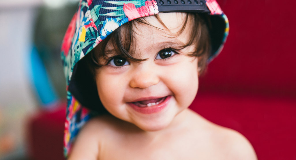 Smiling baby wearing a colorful backward cap, a cheerful portrait for baby name inspiration and parenting content.