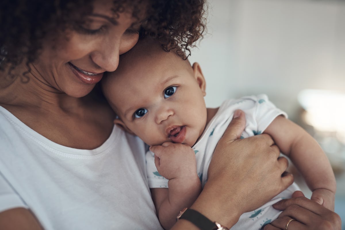 Smiling mother cuddles her baby in a bright home, creating a warm parenting moment focused on infant comfort and care.