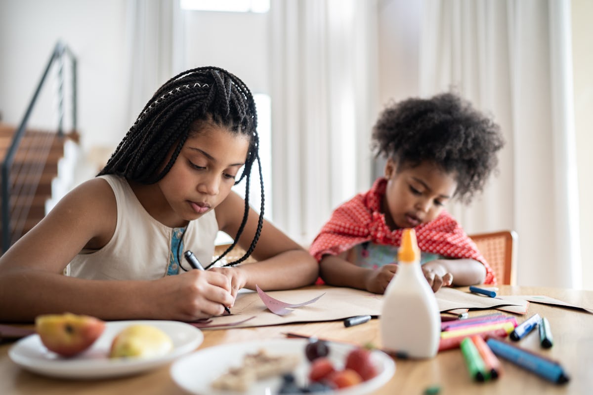 Two children draw and craft at a kitchen table with markers, paper, glue, and snacks, a screen-free summer activity for kids.