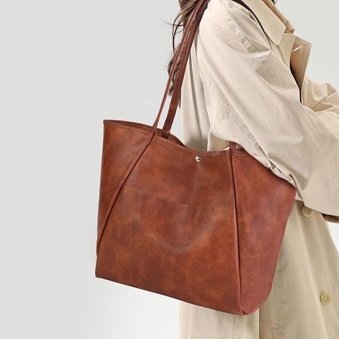 Brown vegan leather tote bag with slim shoulder straps worn over a beige coat, showing a polished everyday handbag for work or errands.
