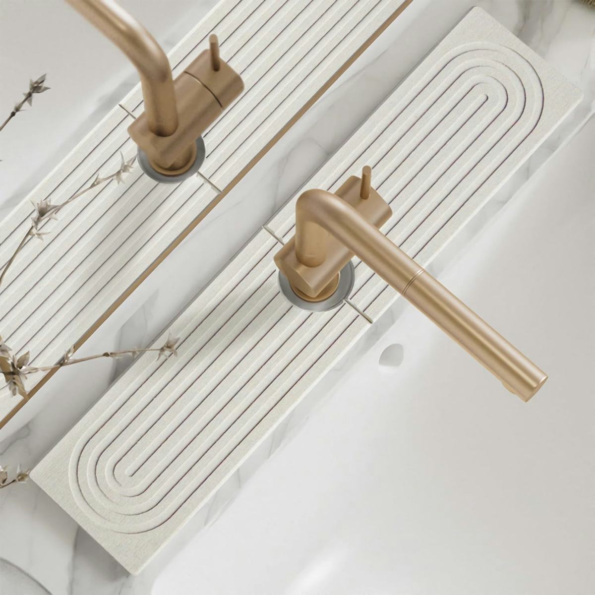 Minimal bathroom sink with brushed gold faucet and white diatomite quick-dry faucet mat on marble-style countertop.