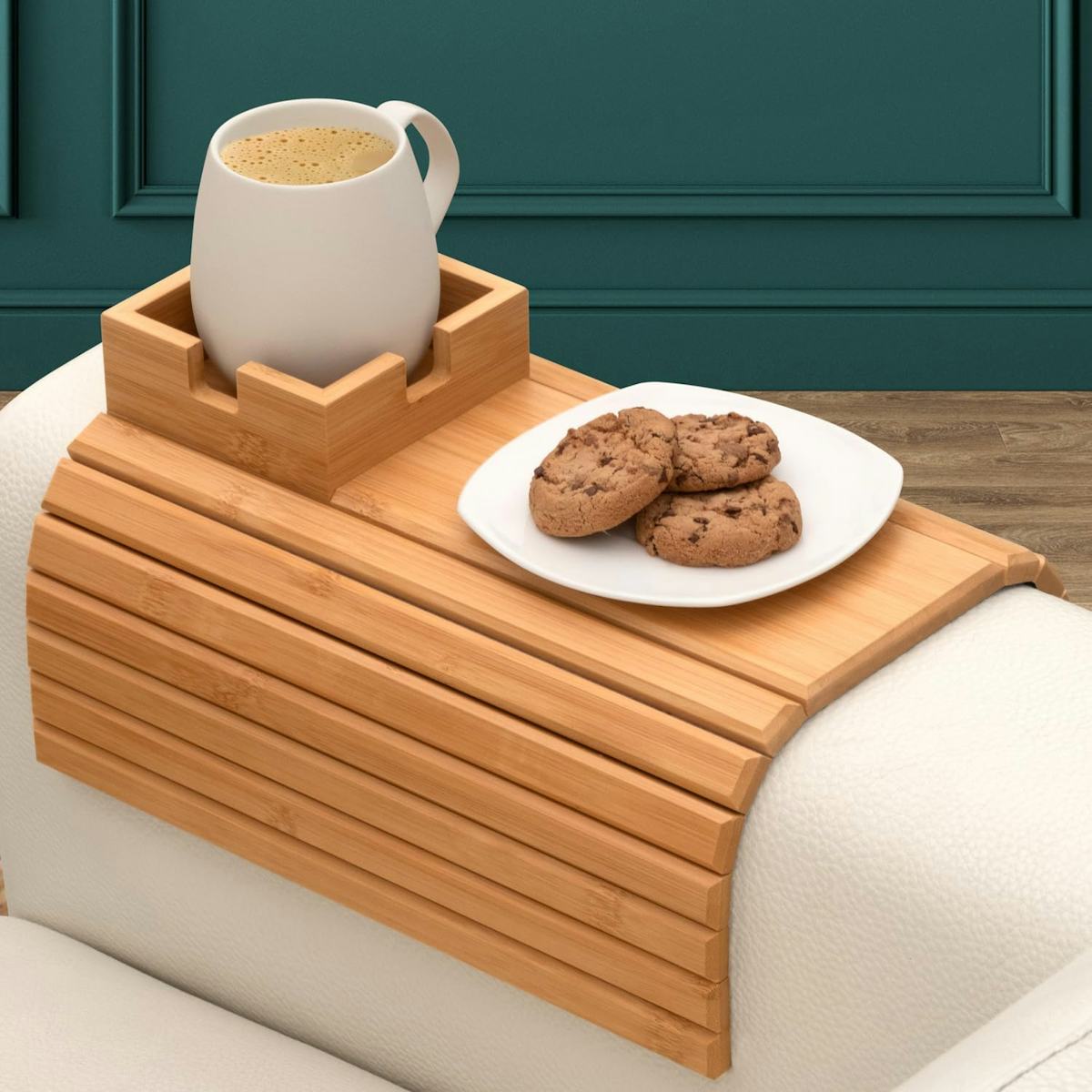 Bamboo couch armrest tray holding a white coffee mug and plate of chocolate chip cookies on a cream sofa.