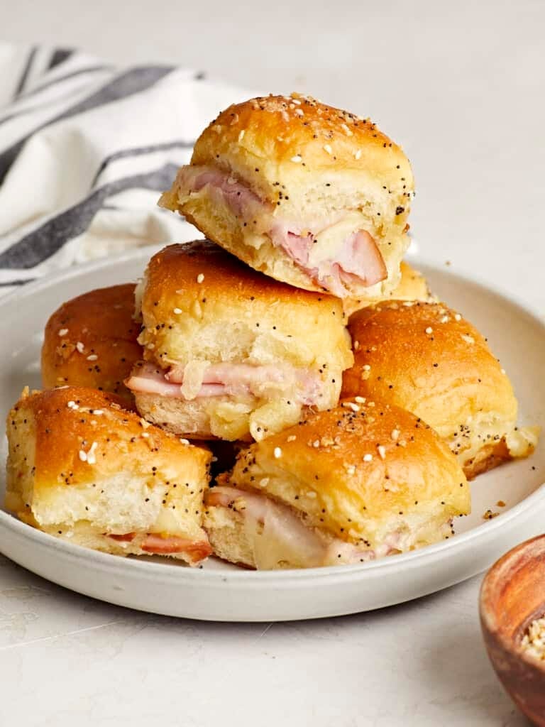 Ham and cheese sliders on Hawaiian rolls stacked on a white plate with melted cheese and everything bagel seasoning.