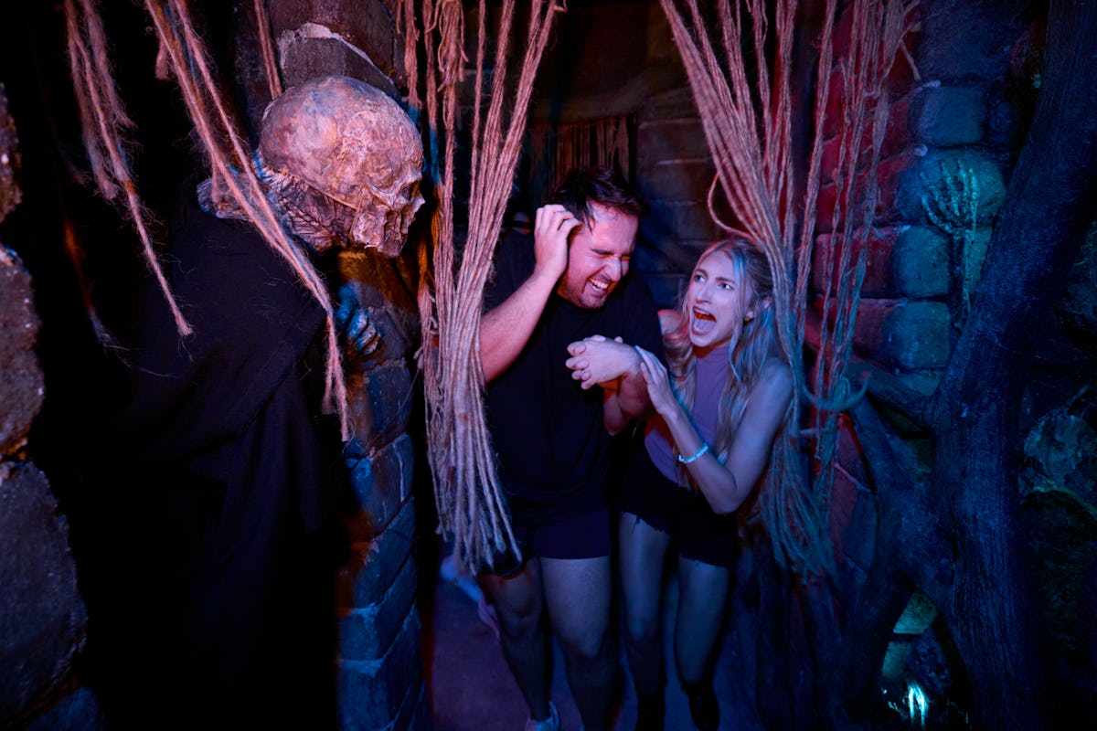 Two guests scream and laugh as a skull-faced scare actor surprises them inside a Halloween Horror Nights haunted house.