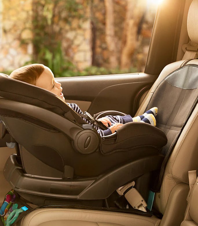 Baby reclining in a rear-facing car seat inside a vehicle, secured with harness straps as warm sunlight shines through the window.