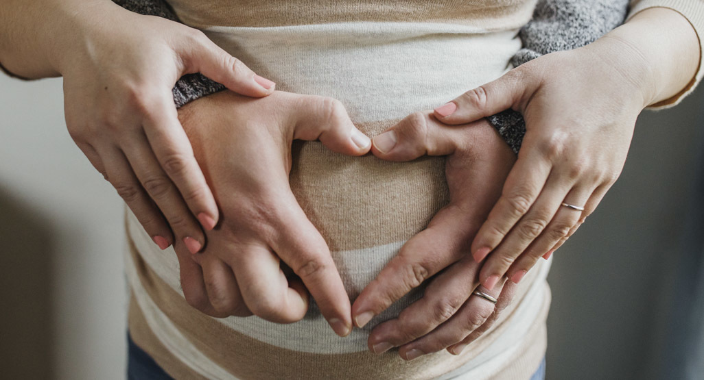 Expectant parents forming a heart with their hands over a pregnant belly, symbolizing family, baby names, and shared parenting choices.