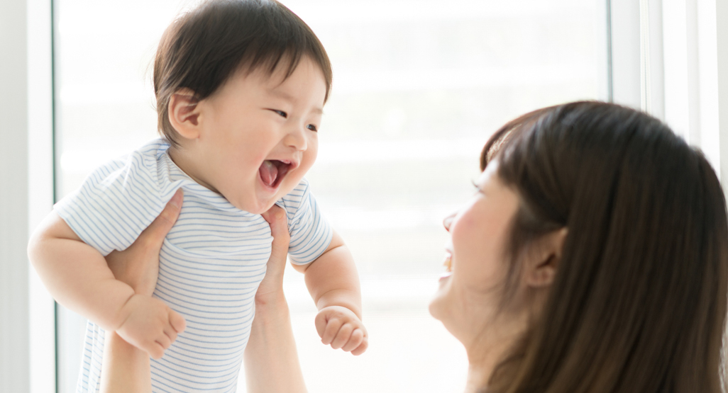 Smiling mother lifting a laughing baby near a bright window, illustrating warmth, family connection, and baby name inspiration.