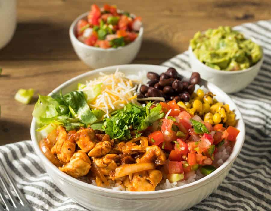 Rice bowl topped with sauced chicken, salsa, black beans, corn, lettuce, cheese, and cilantro.
