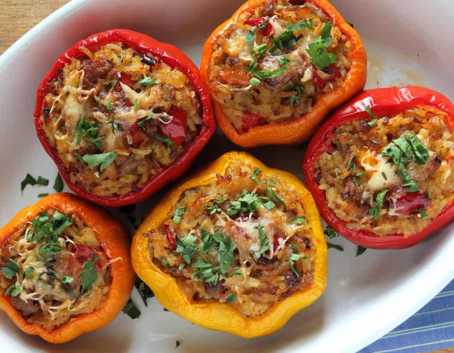Red, orange, and yellow stuffed bell peppers topped with herbs in a white baking dish