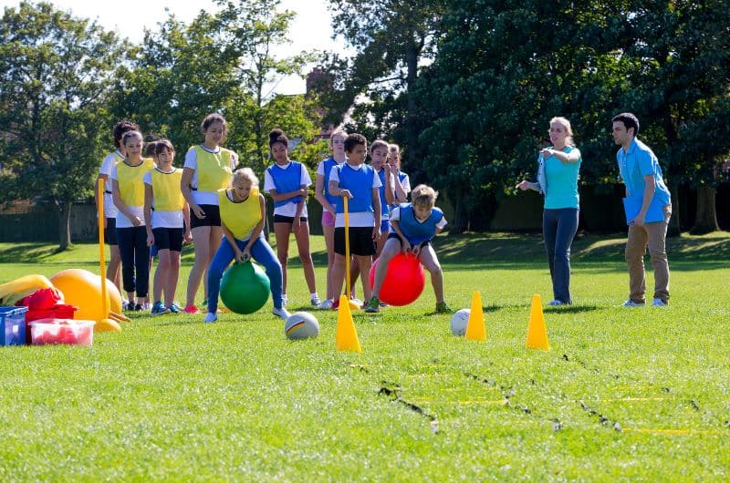 Children and adults on a grassy field with cones and large balls during an outdoor group game