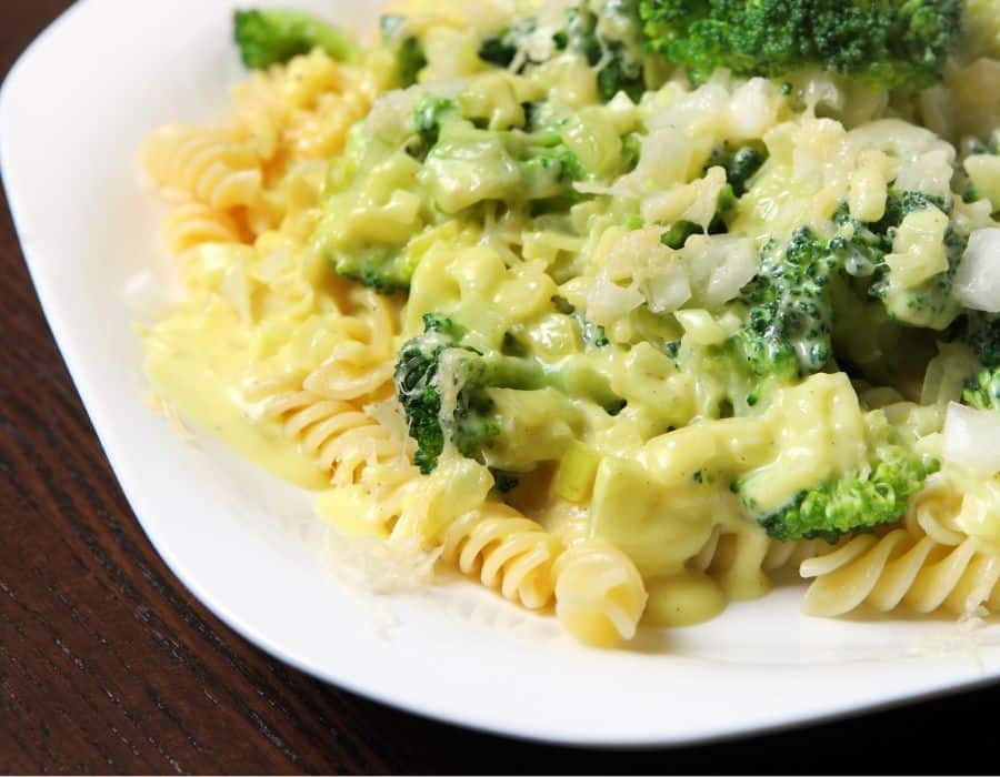 Rotini pasta topped with broccoli and creamy yellow sauce on a white plate