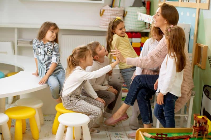 Woman seated with several young children in a colorful classroom or playroom