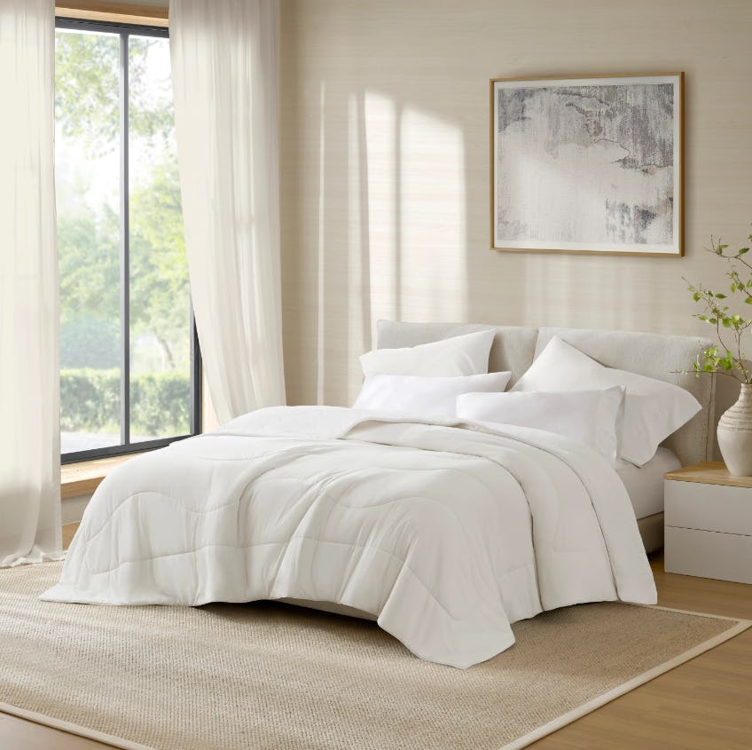 Bright bedroom with white bedding, sheer curtains, abstract wall art, nightstand, vase, and neutral rug.