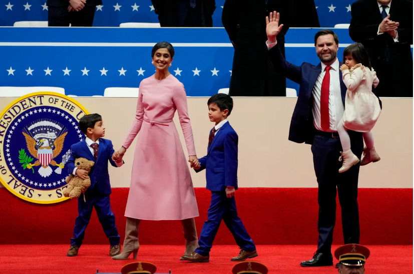 Adults and children walk on a red stage before a blue star backdrop and a partial presidential seal.
