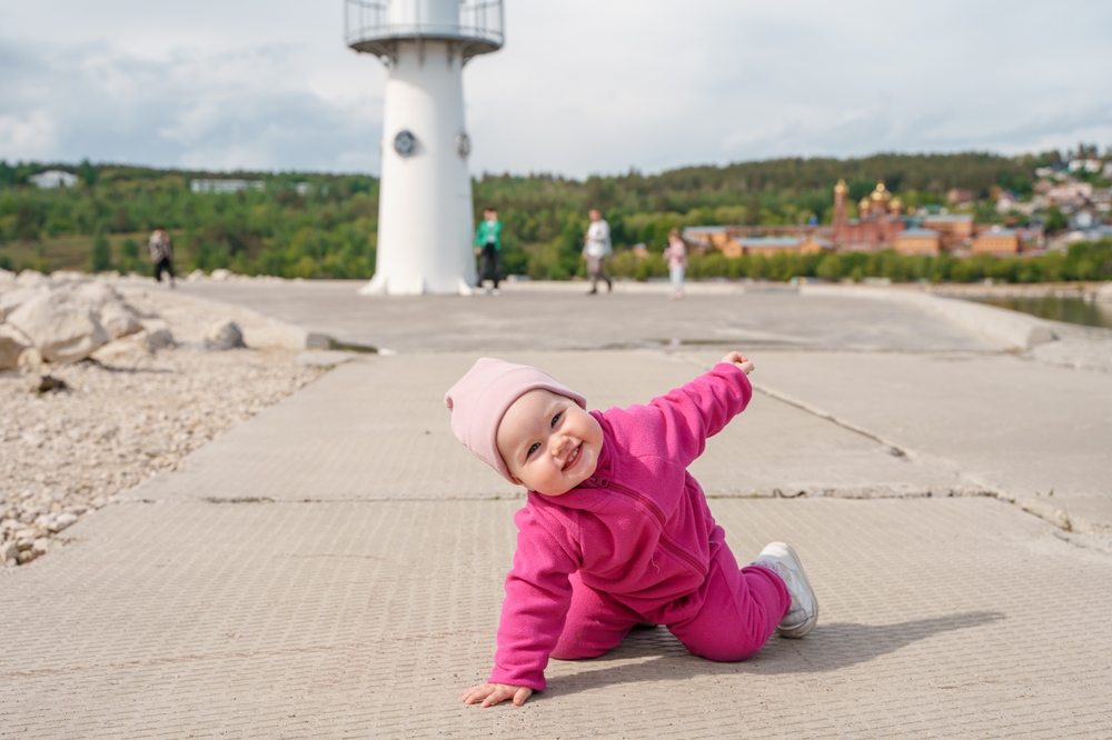Smiling baby in pink crawling on a walkway with a lighthouse in the background