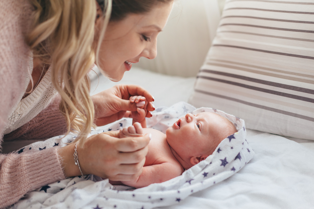 Woman smiling at a baby wrapped in a star-patterned blanket on a bed