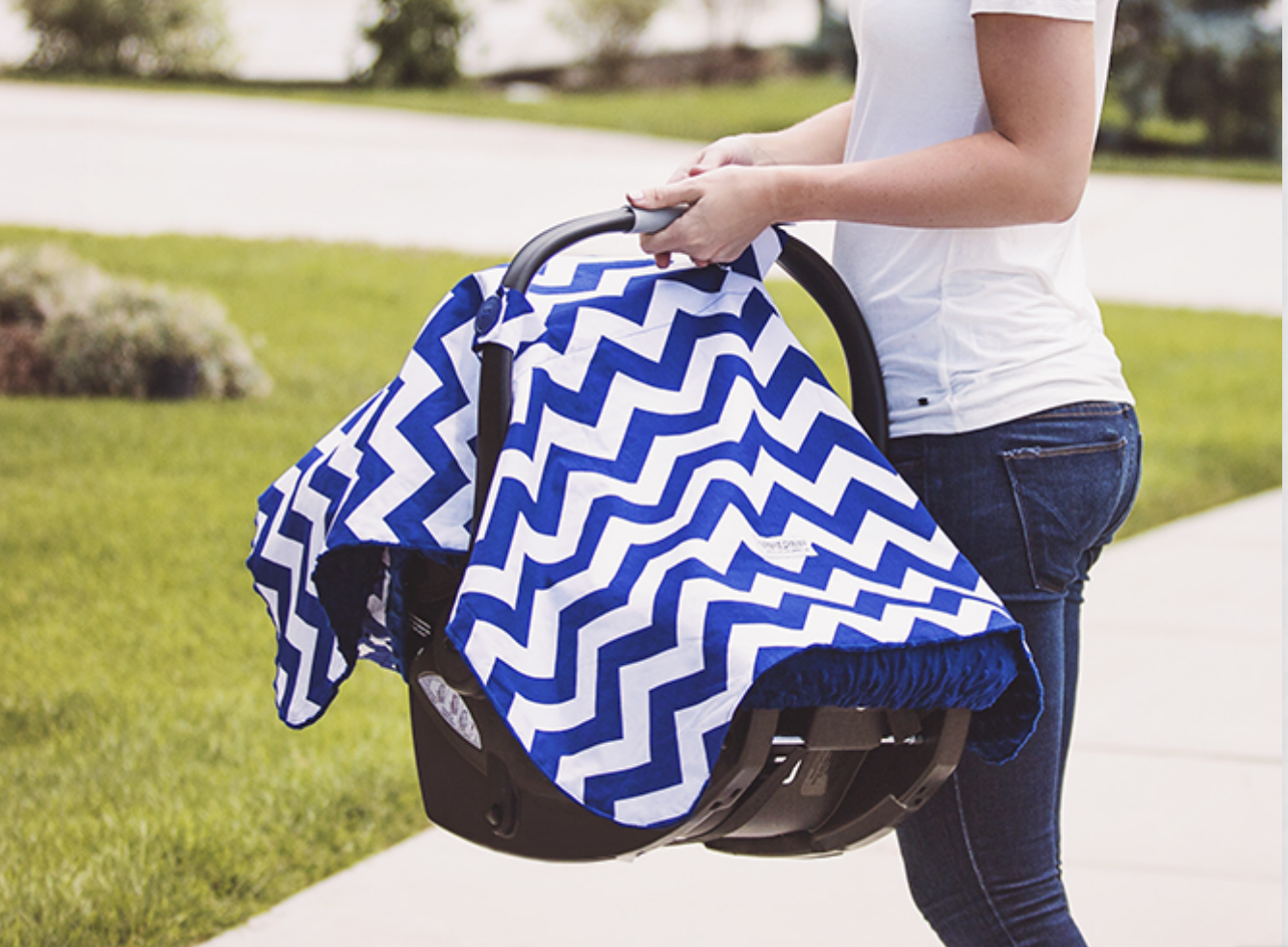 Person holding a baby car seat covered with a blue and white chevron blanket outdoors