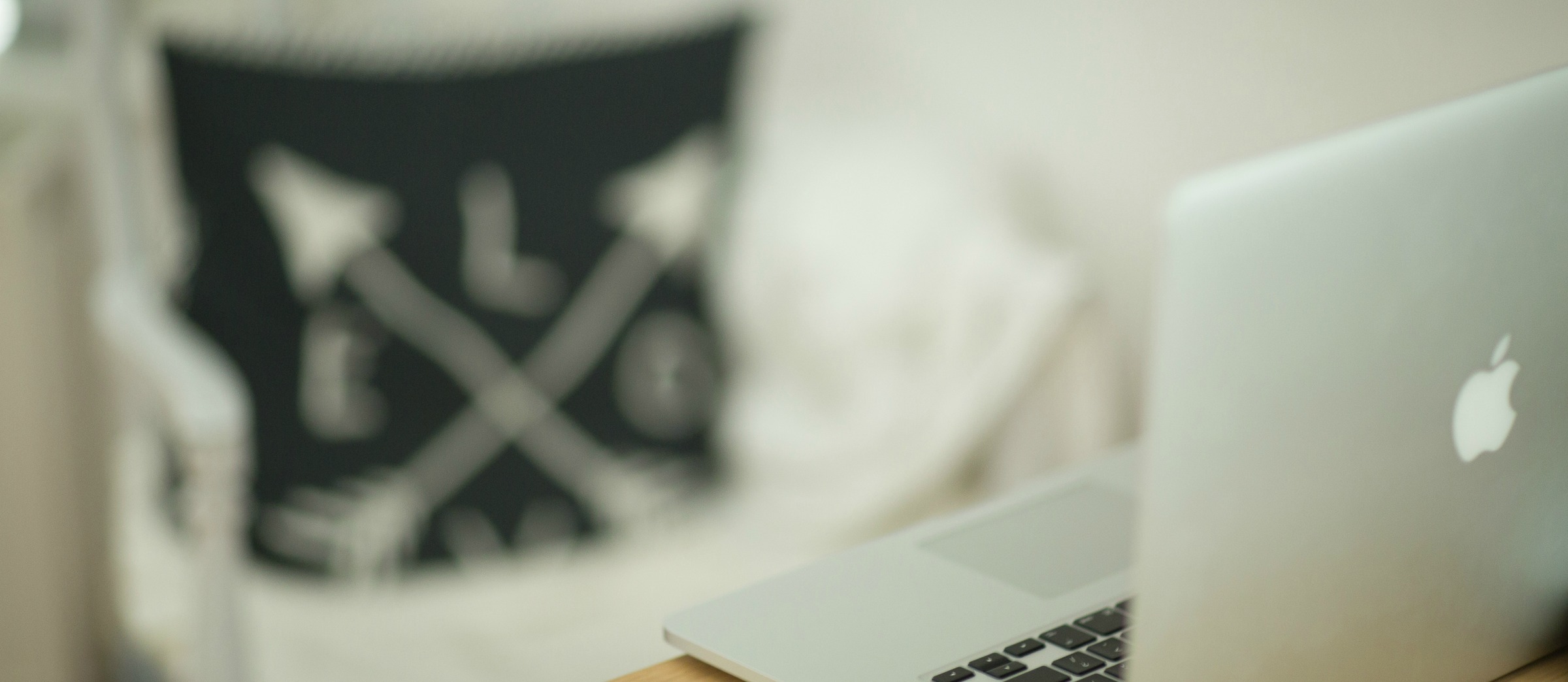 Blurred laptop on a desk beside an out-of-focus chair or bag in a soft indoor setting.
