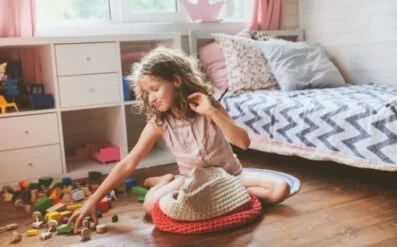 Child sitting on a cushion and reaching for toys on a bedroom floor