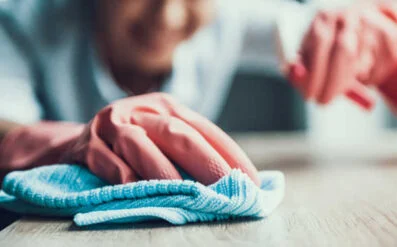 Close-up of a hand wiping a wooden surface with a blue cleaning cloth.
