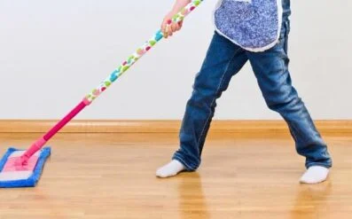 Person in jeans and white socks using a blue floor mop on a wood floor.