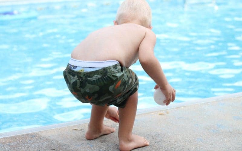 Toddler crouching at the edge of a swimming pool holding a small white object