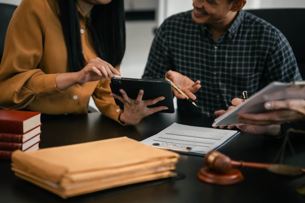 People around a table with a tablet, documents, file folders, books, and a gavel.