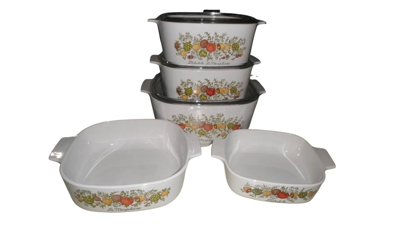 White casserole dishes with fruit-and-herb designs, some stacked with glass lids and two open dishes in front.