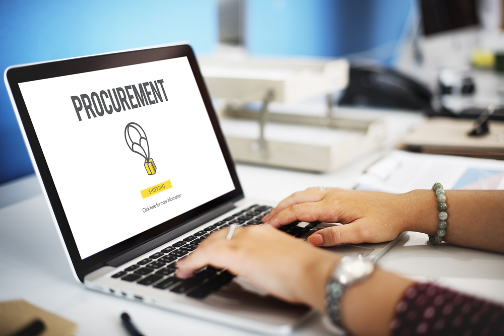 Hands typing on a laptop showing a procurement screen with shipping text
