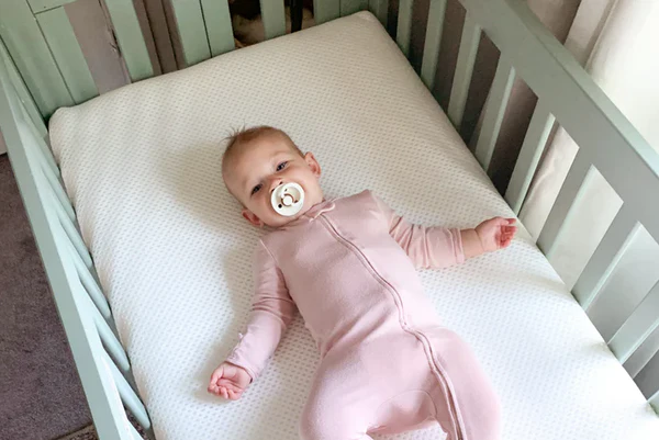 Baby in a pink sleeper lying in a crib with a pacifier