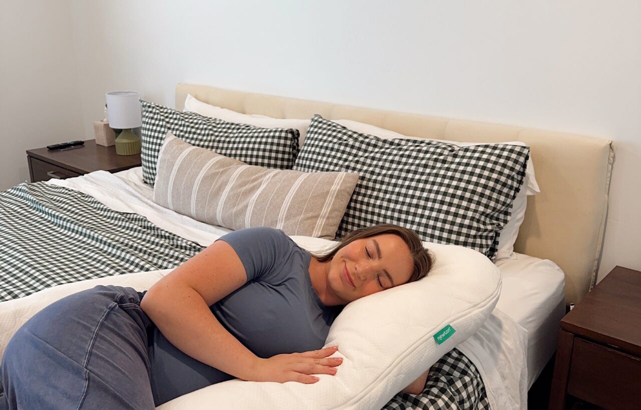 Person lying on a bed hugging a white body pillow beside green checkered bedding.